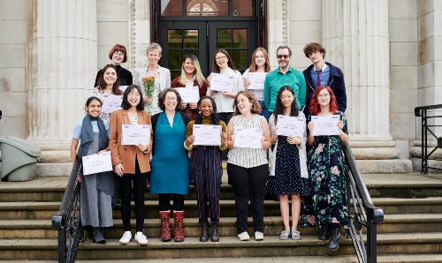 14 students and an academic stood on some steps holding certificates