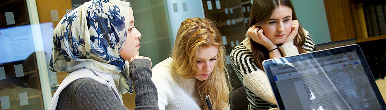 Three students sat at desk in front of laptop